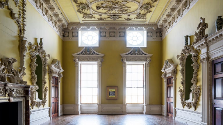 The North Hall at Claydon, Buckinghamshire. A large room with yellow coloured walls covered with intricate carvings